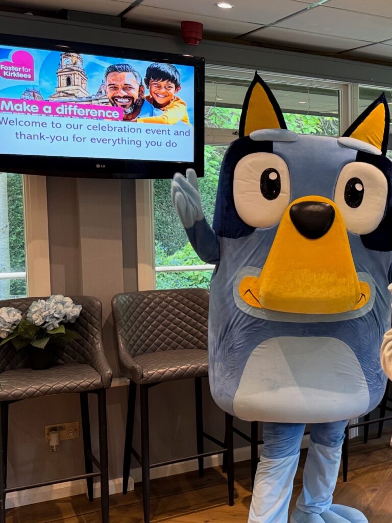 Blue dog mascot waving at a fostering celebration event